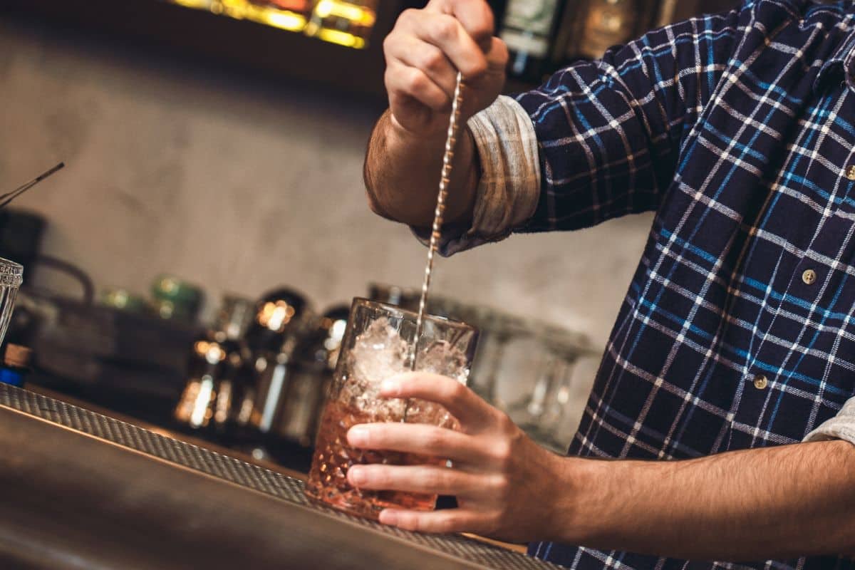 bartender standing at bar counter mixing cocktail with bar spoon